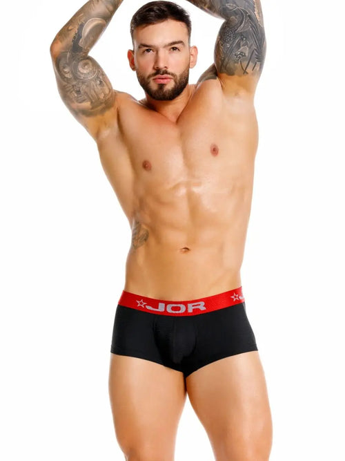 Bearded man with arm tattoos posing in black underwear with a red waistband.