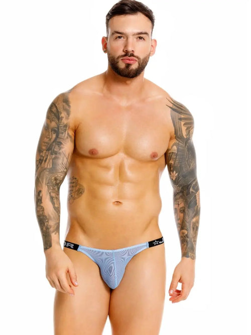 Bearded man with arm tattoos in light blue underwear, white background.