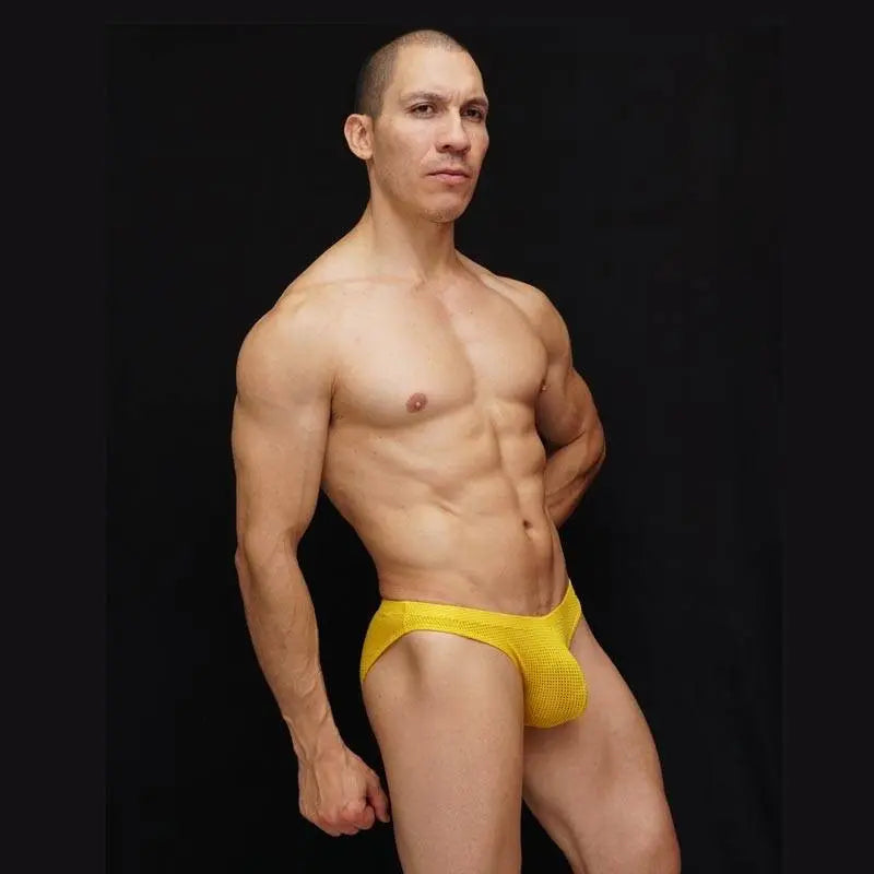 Yellow mesh bikini underwear by Arroyman featuring a snug fit and breathable fabric modeled by a man against a dark background.