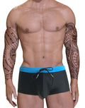 Tattooed man in black swim briefs with a blue waistband.