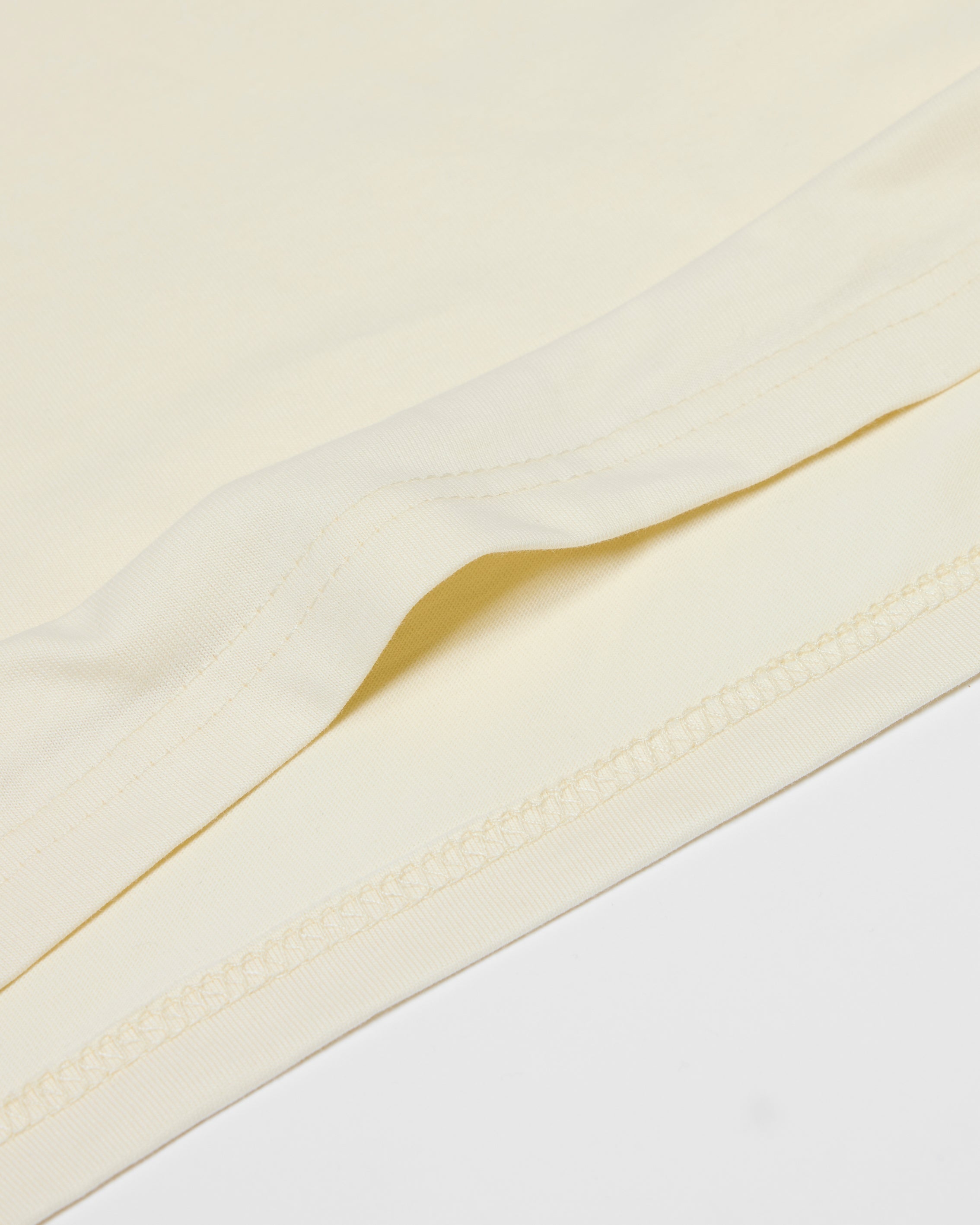 Close-up of a cream-colored Core Tee showing the smooth fabric texture and stitched hem detail.