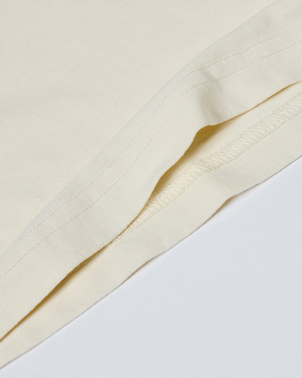 Close-up of a cream-colored t-shirt showing smooth fabric texture and durable double-needle hem stitching.