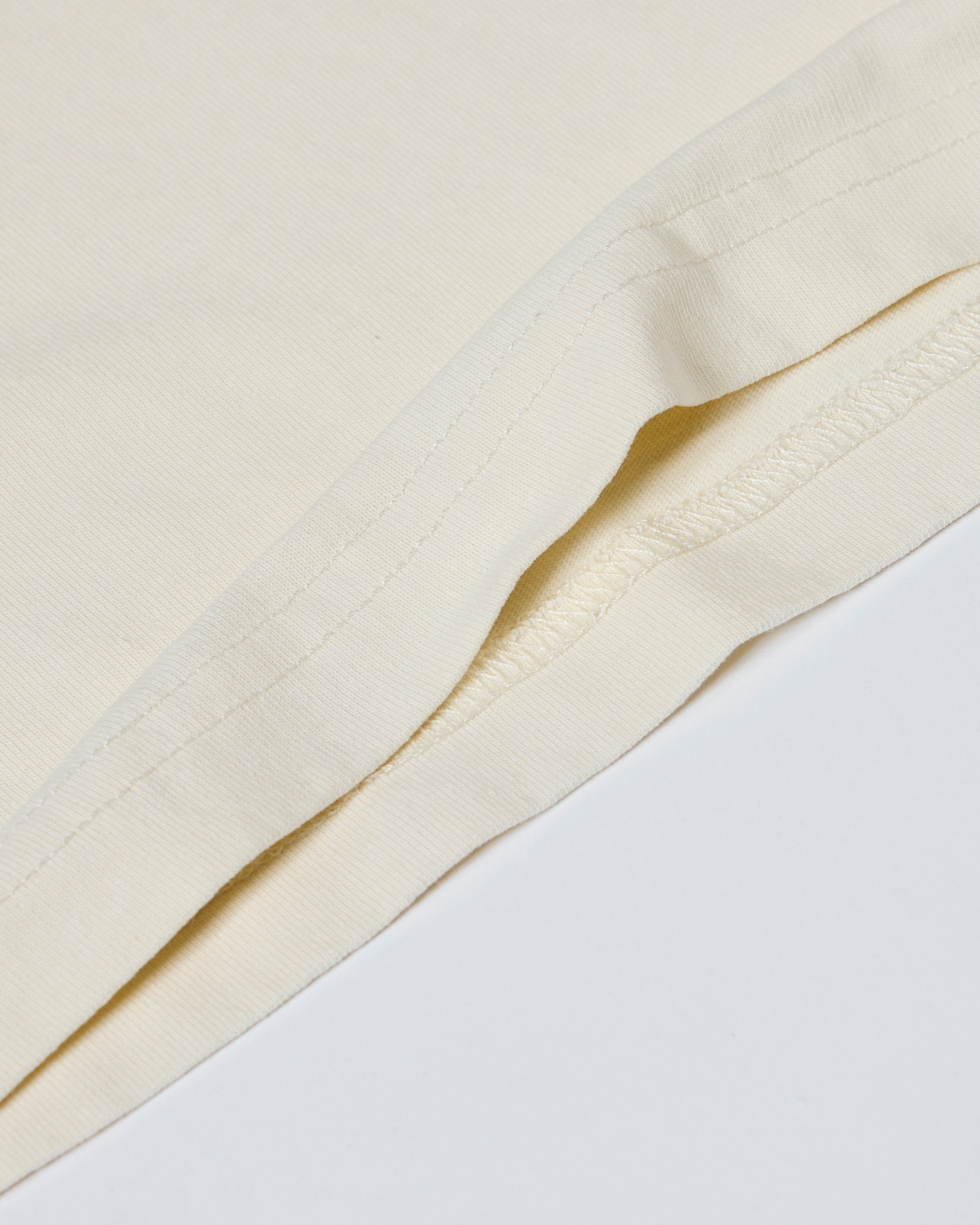 Close-up of a cream-colored t-shirt showing smooth fabric texture and durable double-needle hem stitching.