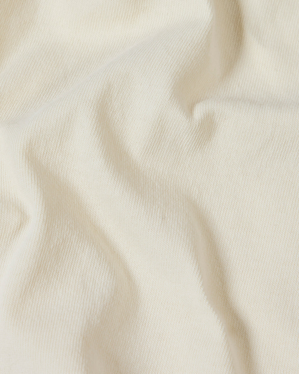 Close-up of a soft, off-white cotton Superior Tee fabric with gentle folds highlighting the knit texture.