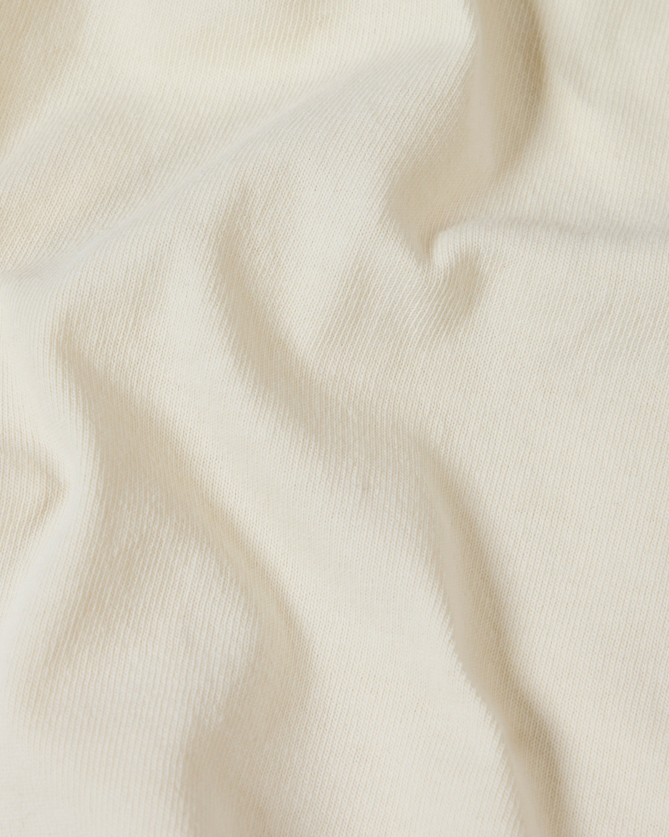 Close-up of a soft, off-white cotton Superior Tee fabric with gentle folds highlighting the knit texture.