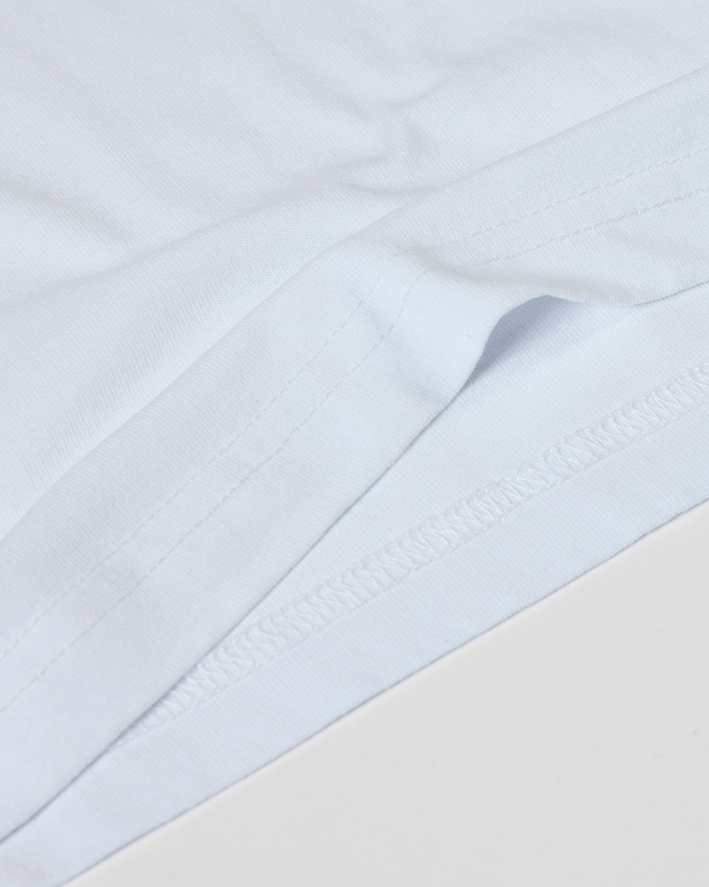 Close-up of a plain white Superior Tee showing high-quality fabric texture and detailed double-needle hem stitching.