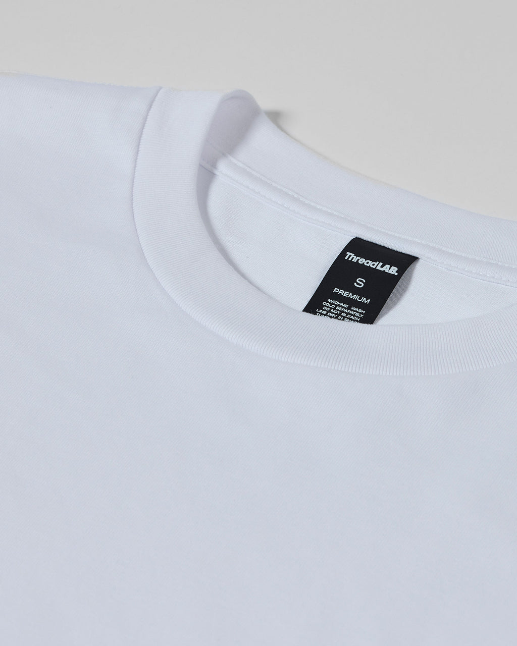 Close-up of a plain white premium crew neck t-shirt with a black ThreadLAB neck label indicating size small.