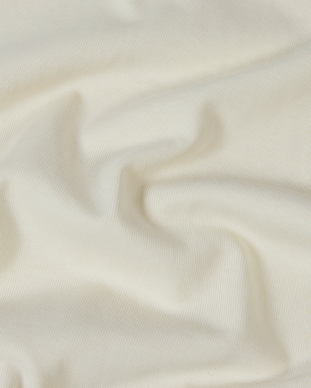 Close-up of soft, off-white premium cotton fabric with gentle folds and a smooth, high-quality knit texture.
