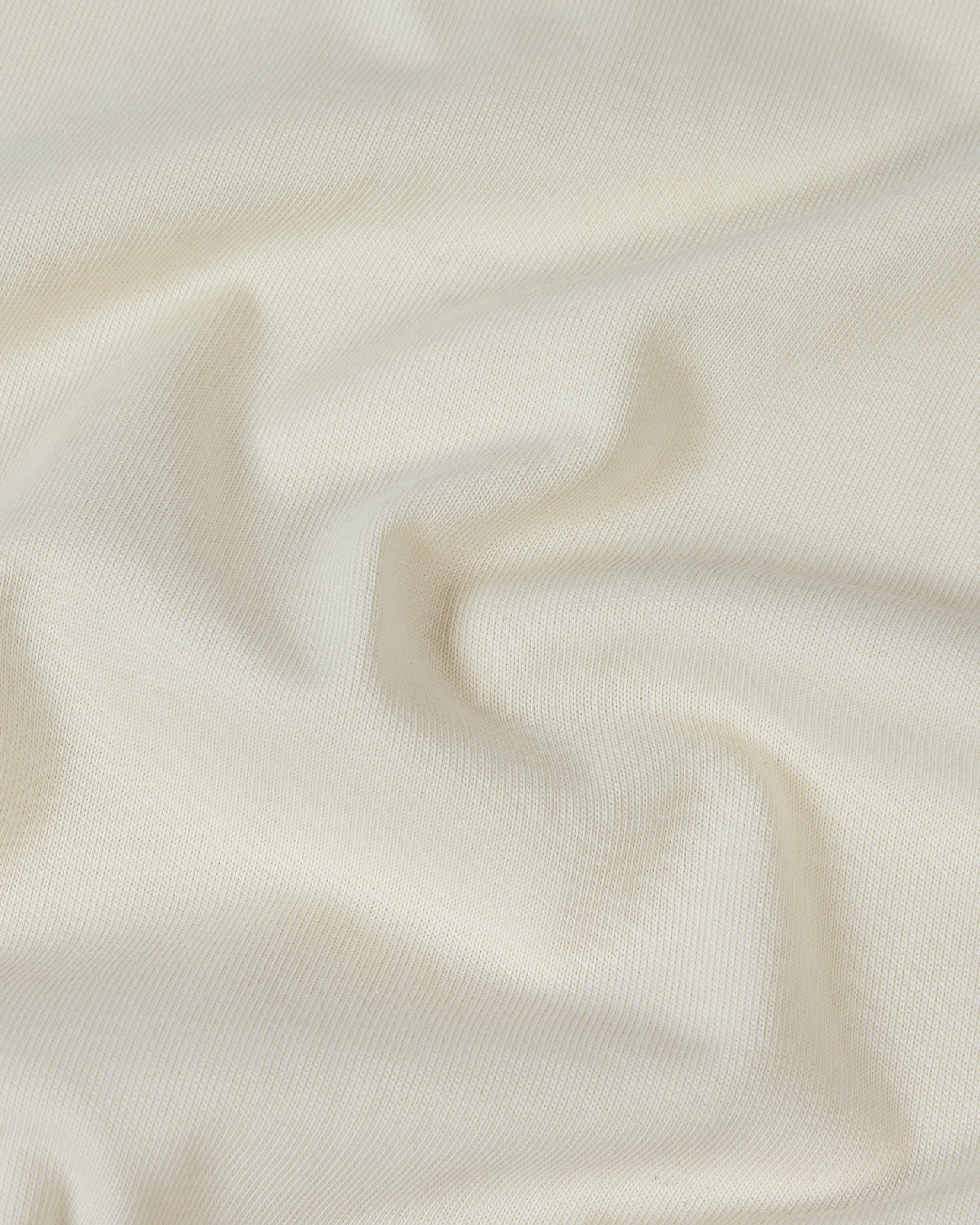 Close-up of soft, off-white premium cotton fabric with gentle folds and a smooth, high-quality knit texture.