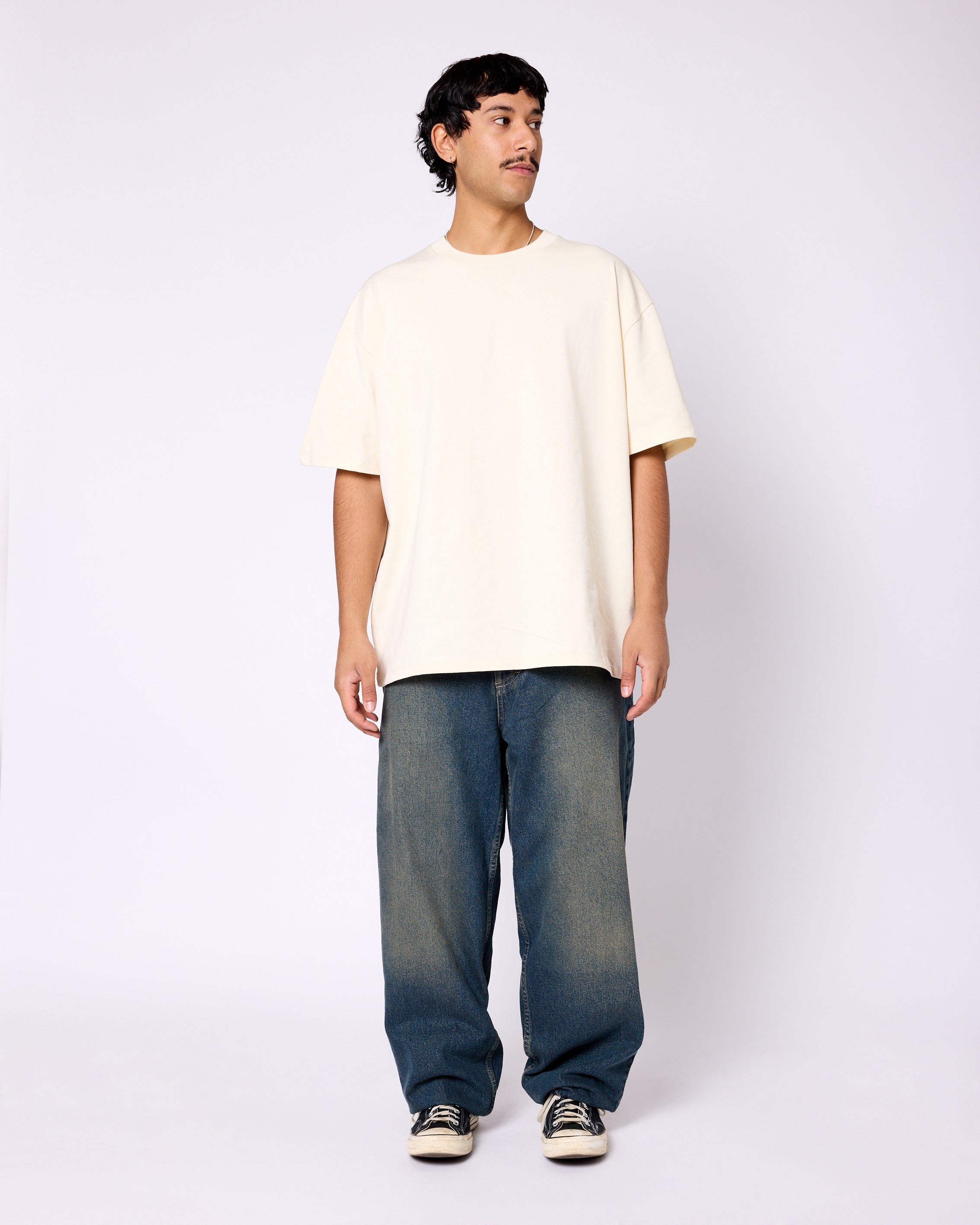 A man wearing an oversized, cream-colored premium crewneck tee with short sleeves against a white background.