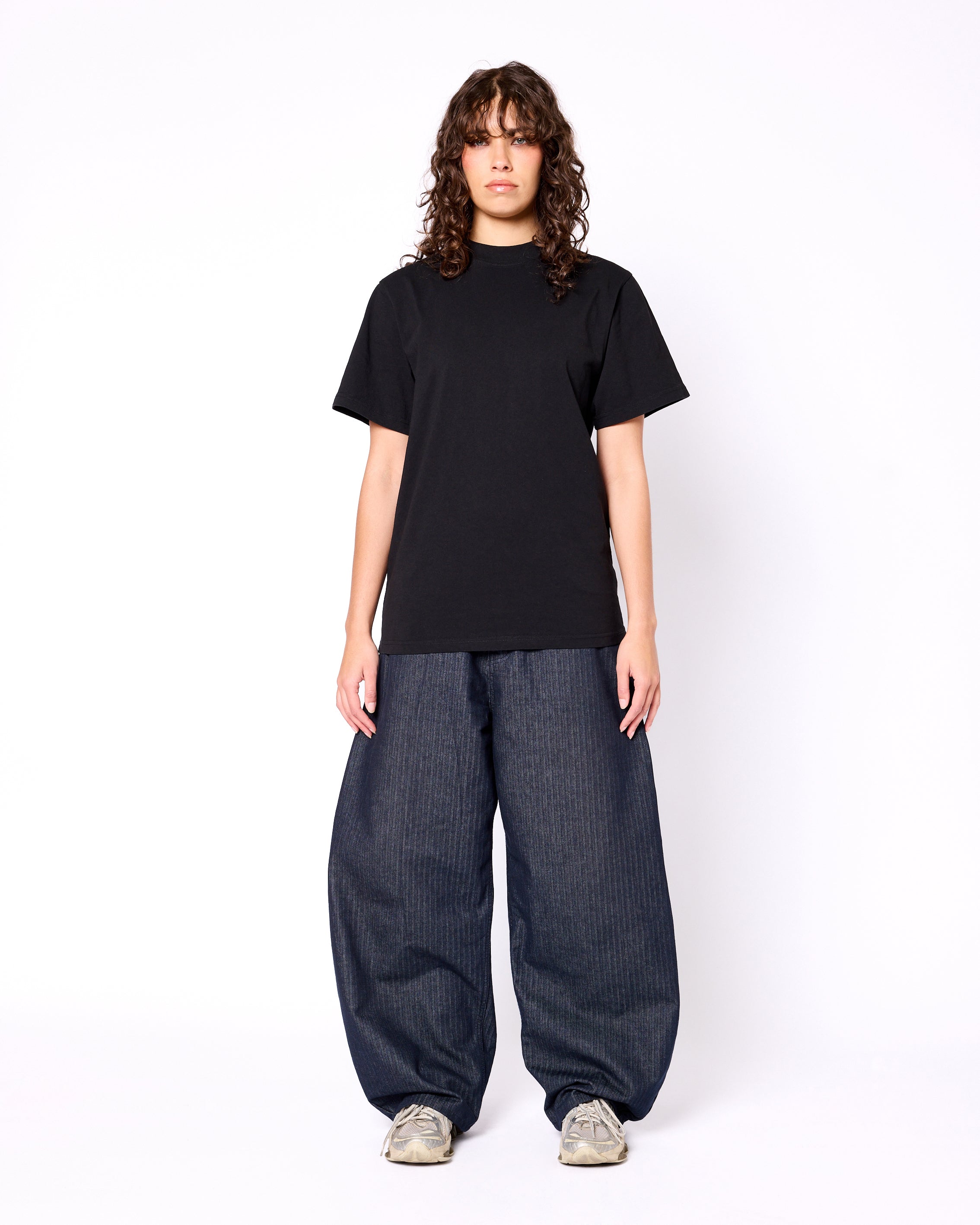 Model wearing a black, heavyweight mock-neck short-sleeve tee paired with baggy, pinstriped navy trousers.