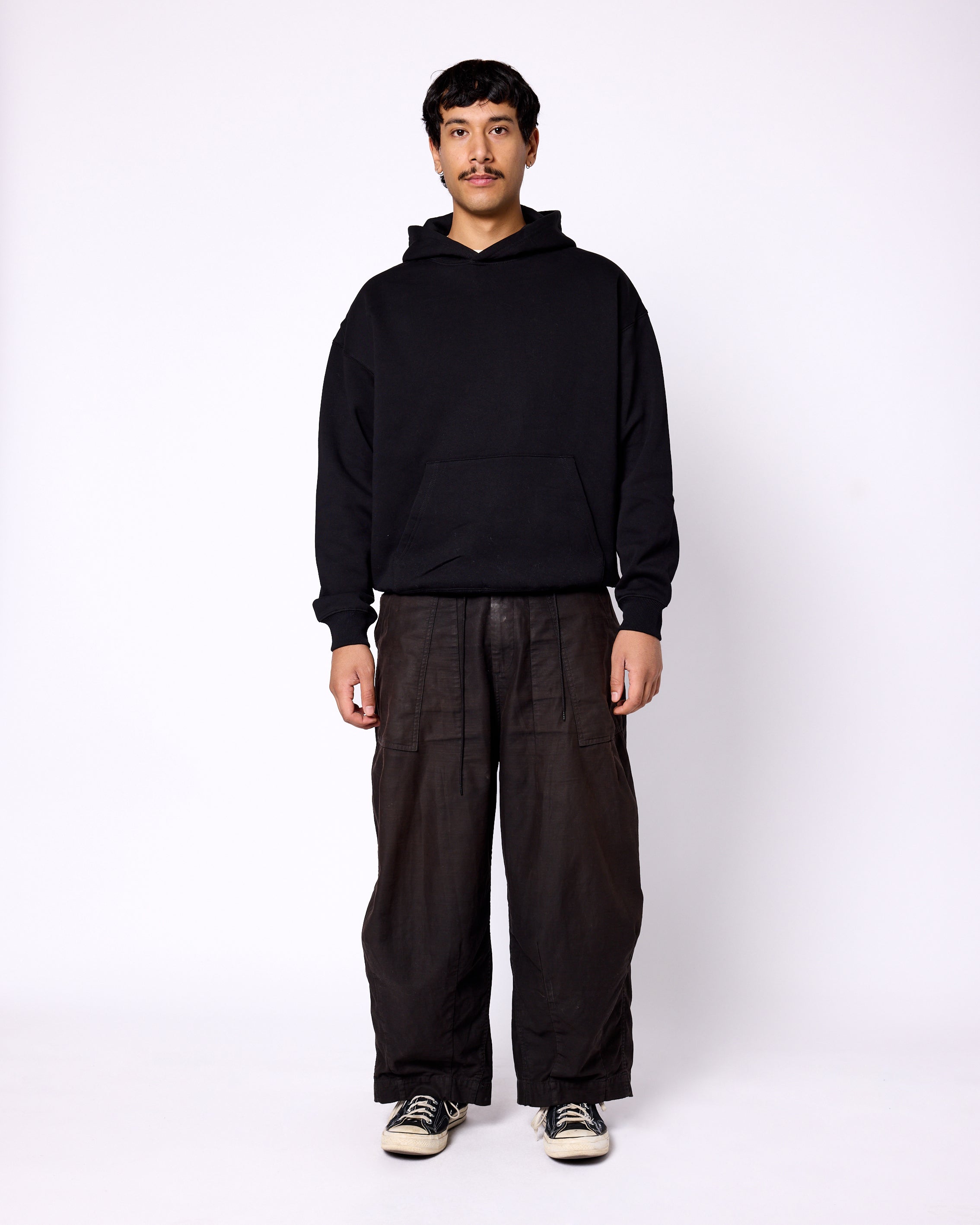 Model wearing a solid black, relaxed-fit pullover hoodie with a spacious front kangaroo pocket.