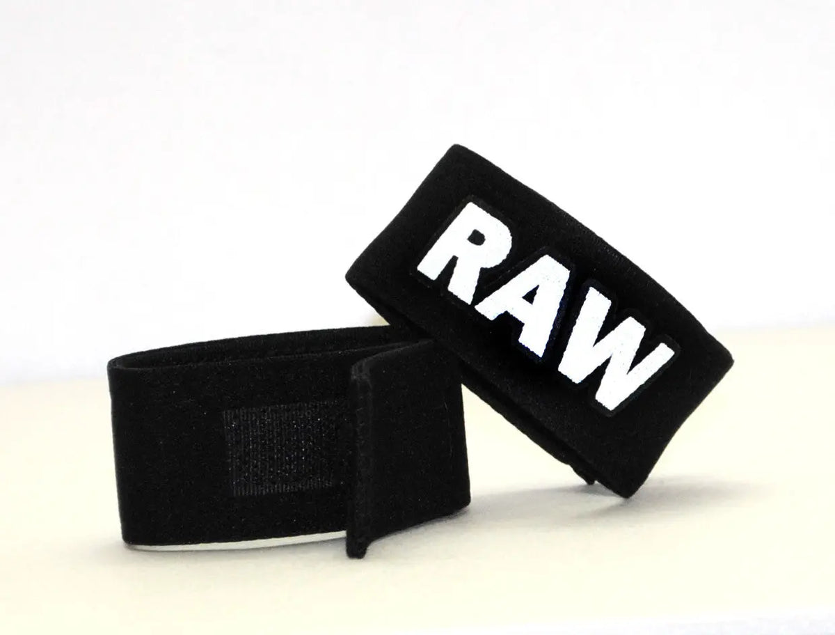 Two black wrist wraps on a white surface, one showing white "RAW" text.