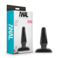 Black plastic anal plug with rounded tip and flat base next to packaging from anal adventures basic anal plug medium m