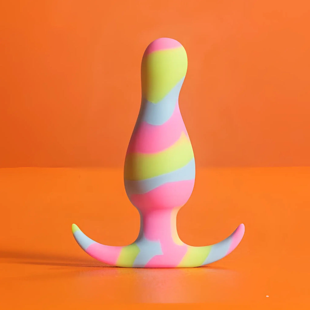 A vibrant rainbow-striped silicone butt plug with a curved base from avant avant kaleido lime collection