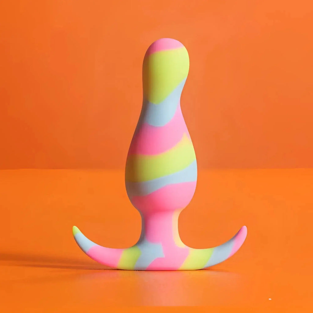 A vibrant rainbow-striped silicone butt plug with a curved base from avant avant kaleido lime collection