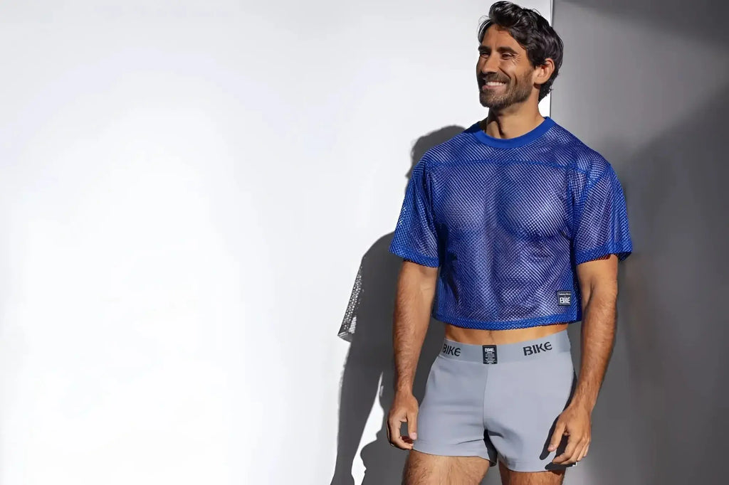 Man wearing a bright blue mesh crop top and light grey Bike brand boxer briefs.
