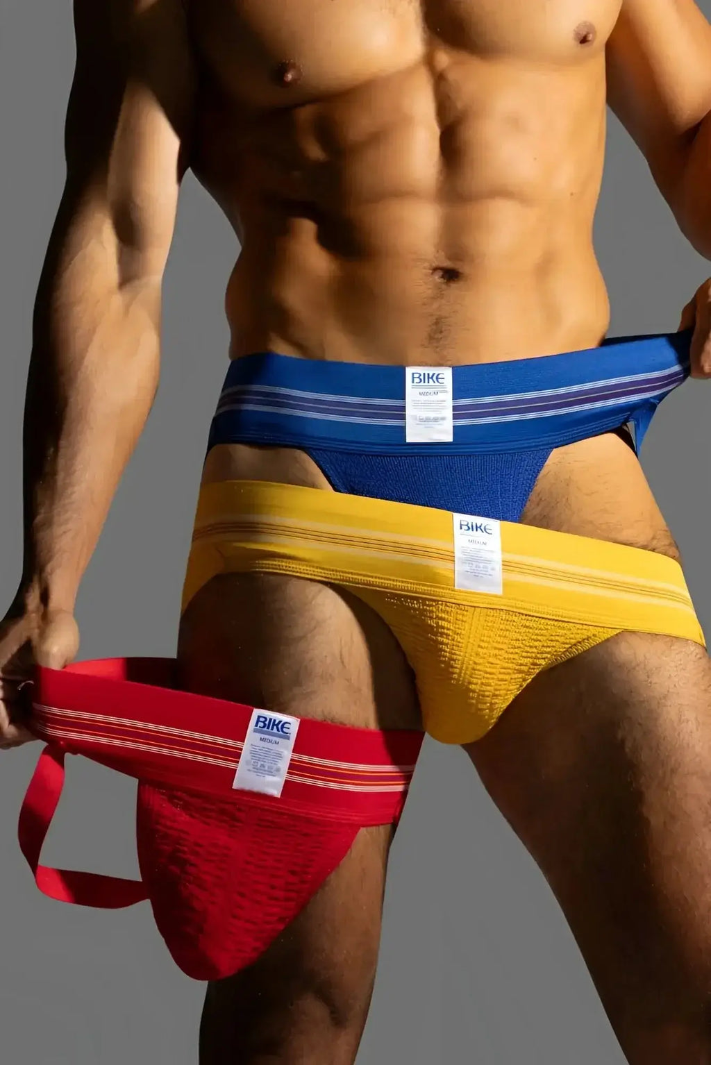 BIKE Athletic BAS306 Original Number 10 jockstrap in royal, yellow, and red. Lifestyle shot of a man wearing jockstraps.
