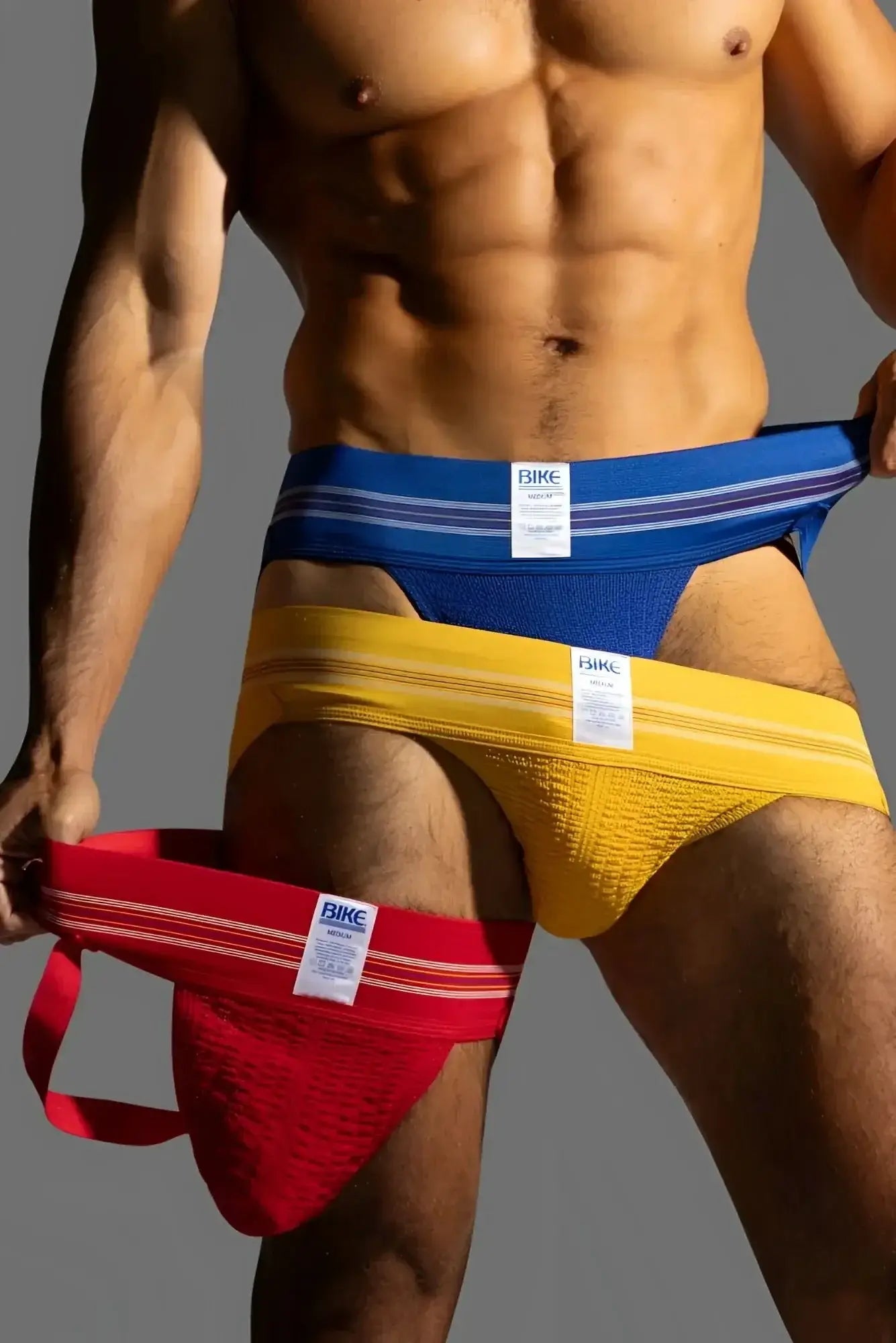 BIKE Athletic BAS306 Original Number 10 jockstrap in royal, yellow, and red. Lifestyle shot of a man wearing jockstraps.