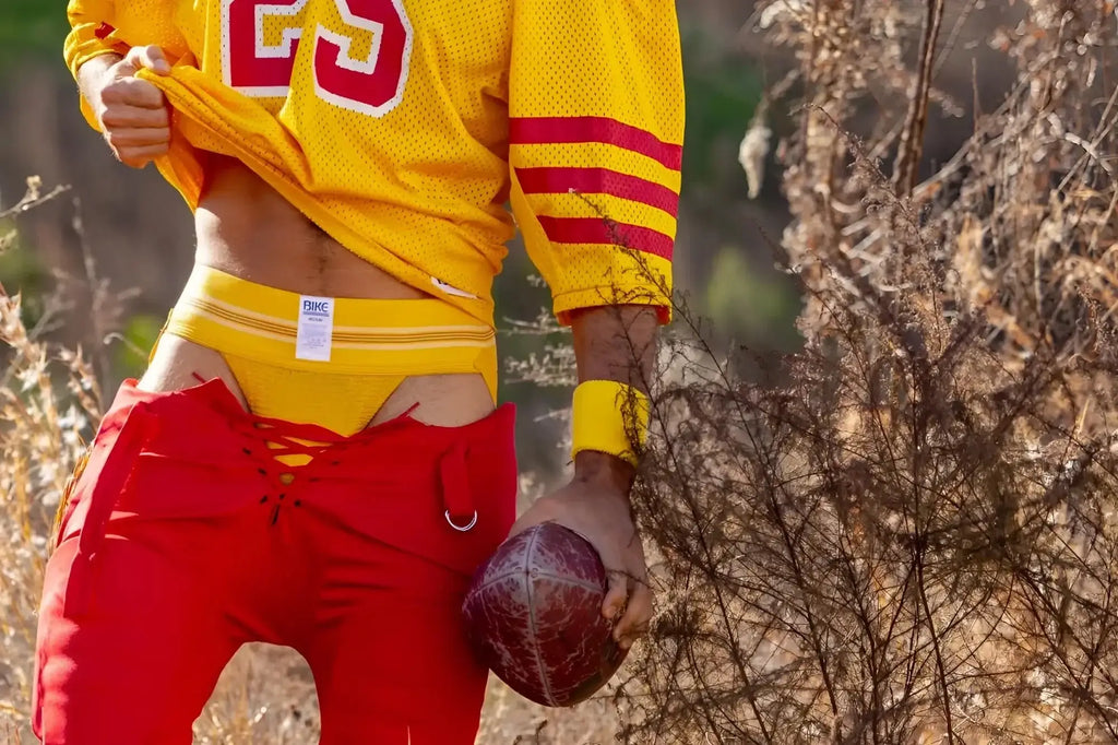 BIKE Athletic BAS306 Original Number 10 yellow jockstrap in a football-themed lifestyle shot.