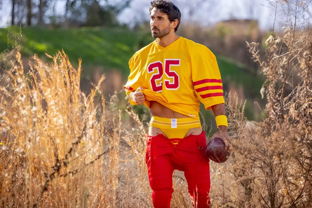 Lifestyle shot of a man wearing a yellow BIKE Athletic BAS306 jockstrap and a football jersey in a field.
