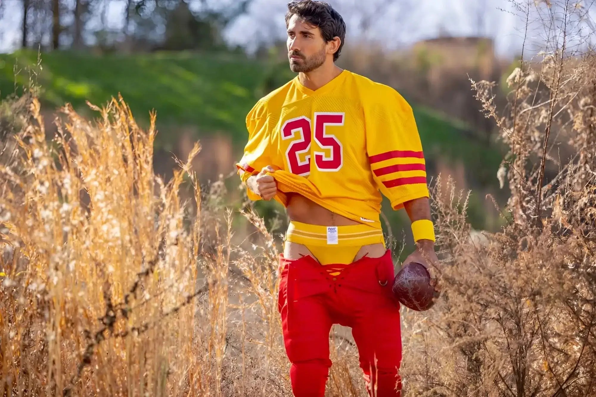 Lifestyle shot of a man wearing a yellow BIKE Athletic BAS306 jockstrap and a football jersey in a field.