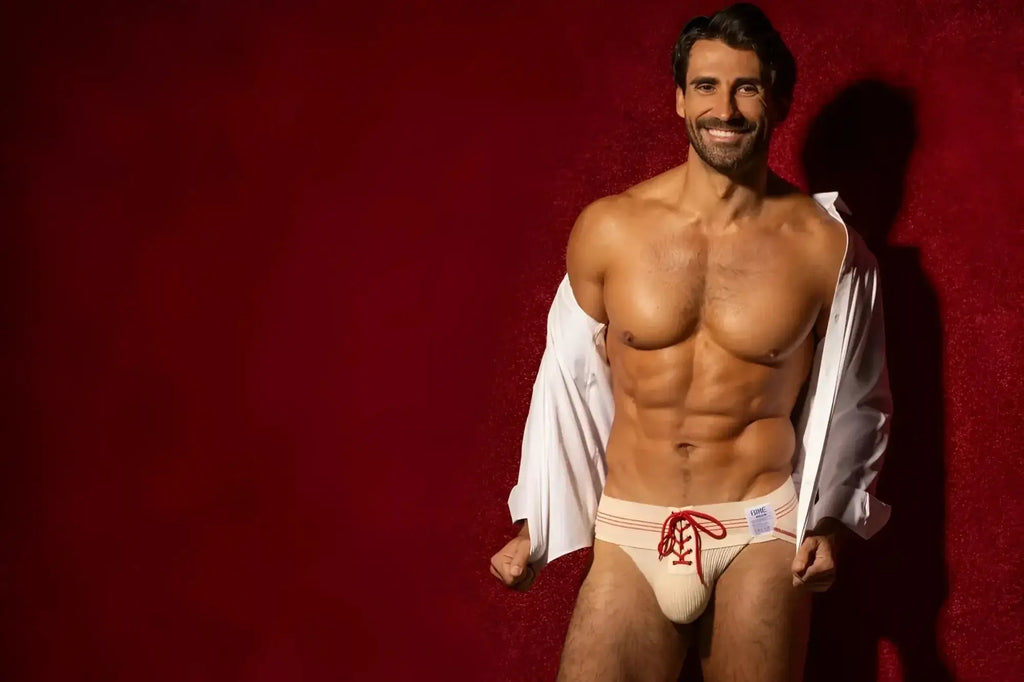 Model wearing BIKE Athletic BAS343 vintage lace-up jockstrap in vintage cream, lifestyle shot against red background.