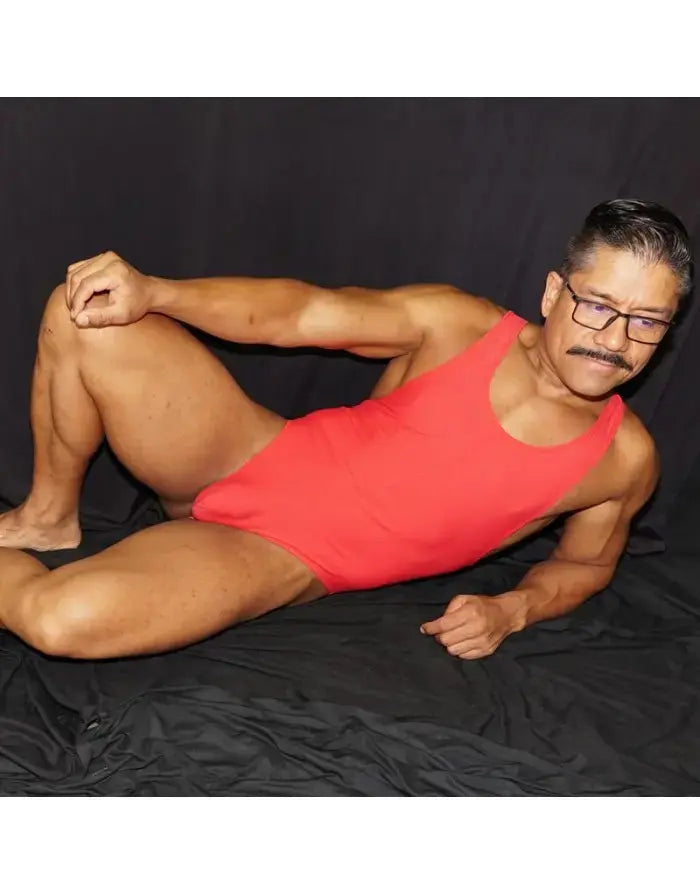 Red bodysuit thong made of stretchy material featuring a sleeveless design modeled by a man against a dark background by Arroyman