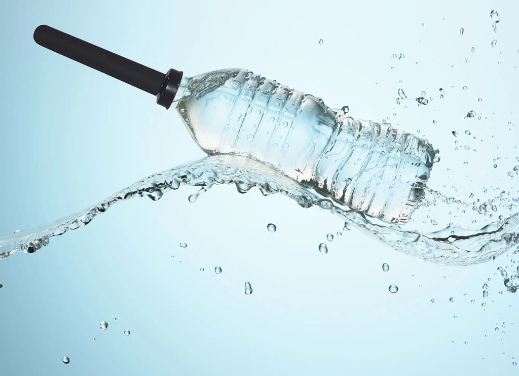 Clear plastic water bottle with black cap and ridged texture partially submerged in splashing liquid for boneyard the skwert 5 pc douche kit