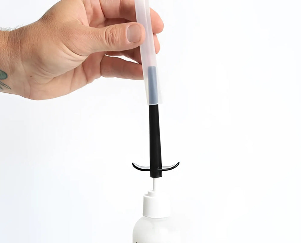 Transparent plastic boneyard skwert lube injector syringe with black plunger and white bottle below
