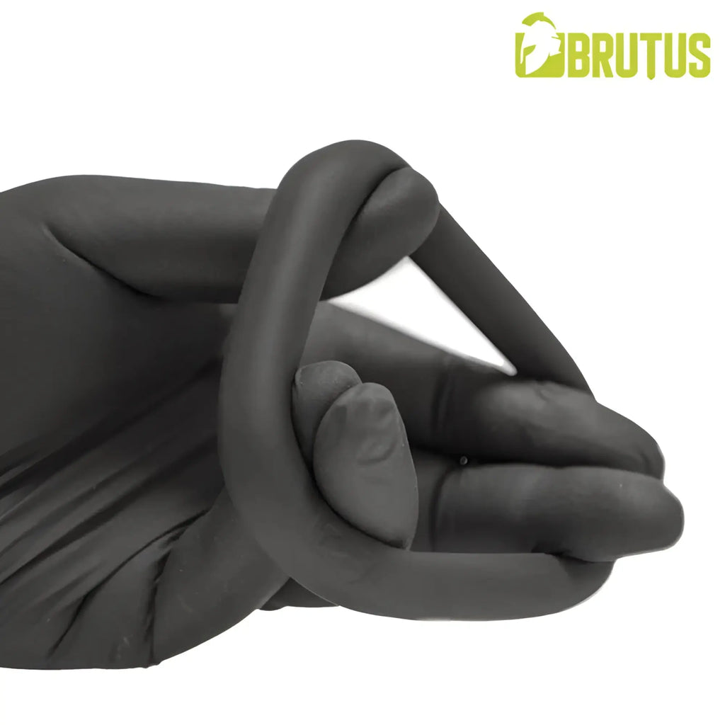 A black latex glove held in hand next to the brutus hypersoft silicone ergo cockring for ergonomic comfort