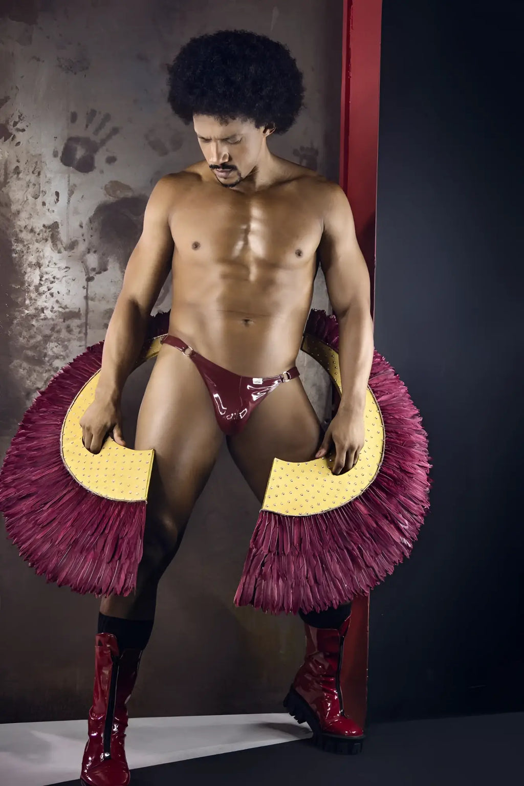 A shiny maroon latex dom thong with bold fringed magenta and yellow circular accessories on each side candyMan 99819