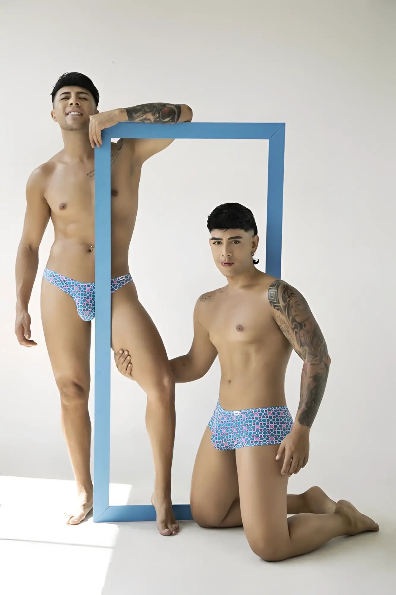 Lifestyle shot of two models wearing blue CandyMan 99922 printed trunks in a studio setting.