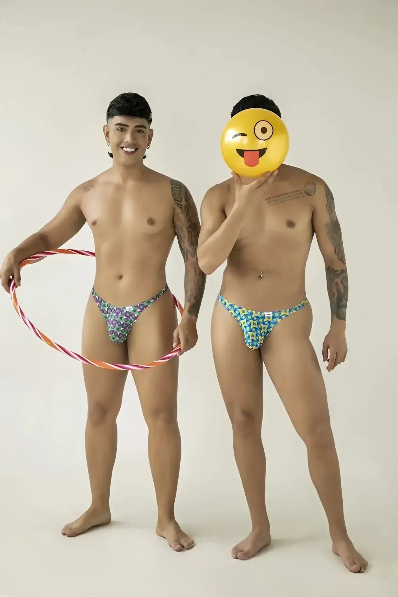 Two men posing in CandyMan 99924 printed purple thongs. Lifestyle shot featuring hula hoop and smiley face balloon.