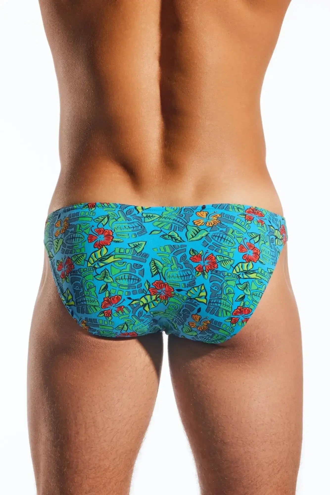 Cocksox cx01 brief vibrant turquoise swim trunks with bold red hibiscus flowers green leaves and stylized ancient masks