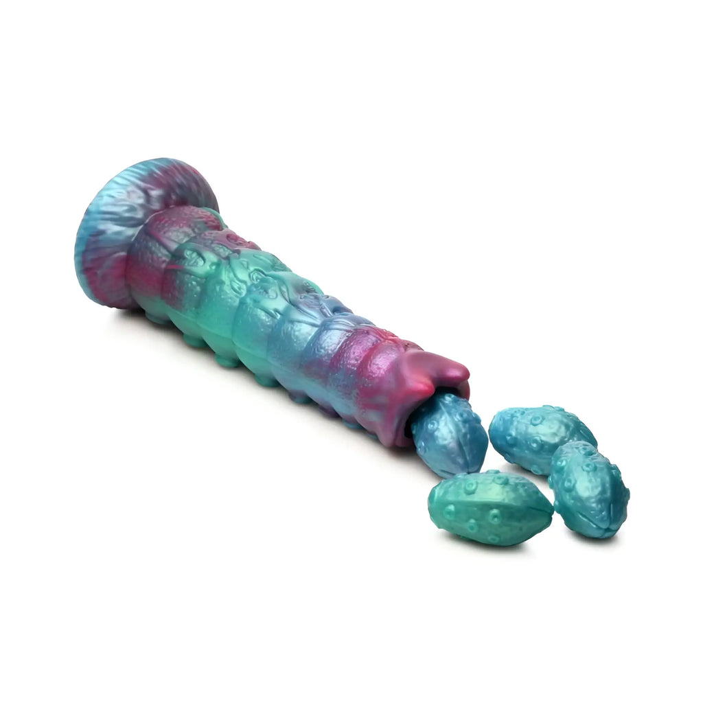 A vibrant gradient-colored silicone caterpillar-shaped dildo with textured surface and teal egg-like pieces nearby