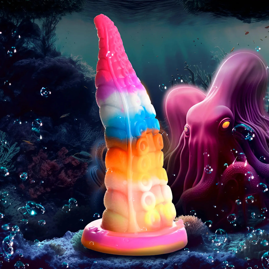 A vibrant rainbow-colored silicone Creature Cocks Luminoctopus GITD tentacle dildo with textured surface and glowing base