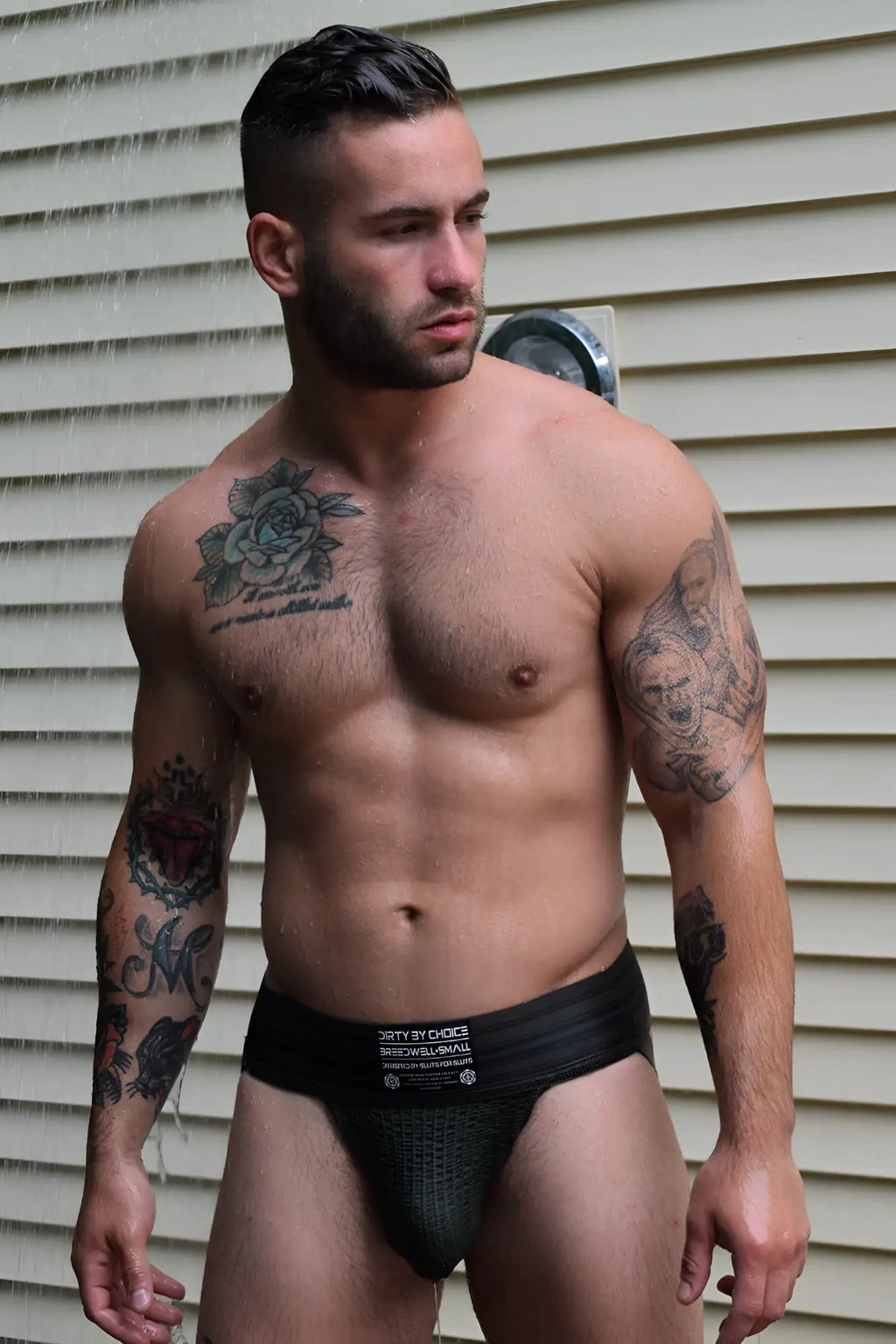 Black mesh briefs with a white label featuring text and logos from the cumdump jock army green collection