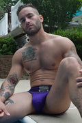 Purple mesh briefs with a black waistband featuring white text and logos from cumdump jock purple collection