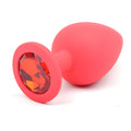 A vibrant coral-red large silicone anal plug with a faceted orange gemstone set in its circular base