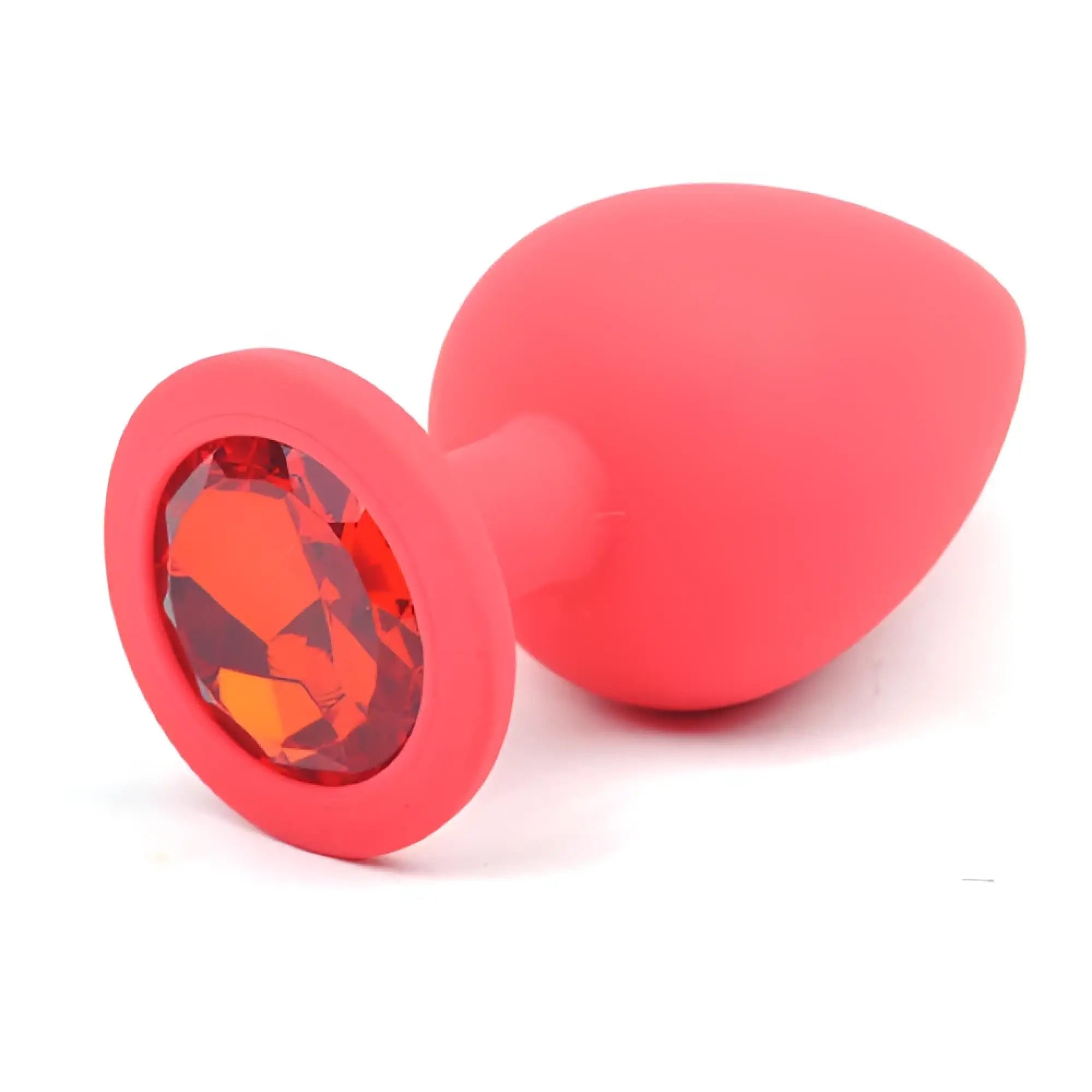 A vibrant coral-red large silicone anal plug with a faceted orange gemstone set in its circular base