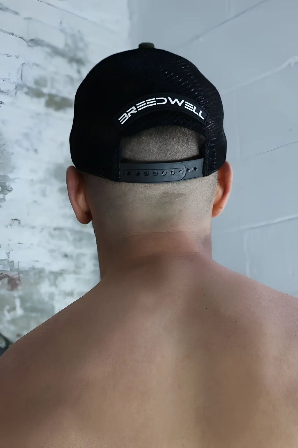 Back view of black mesh dirty trucker hat with white breedwell lettering across the back panel