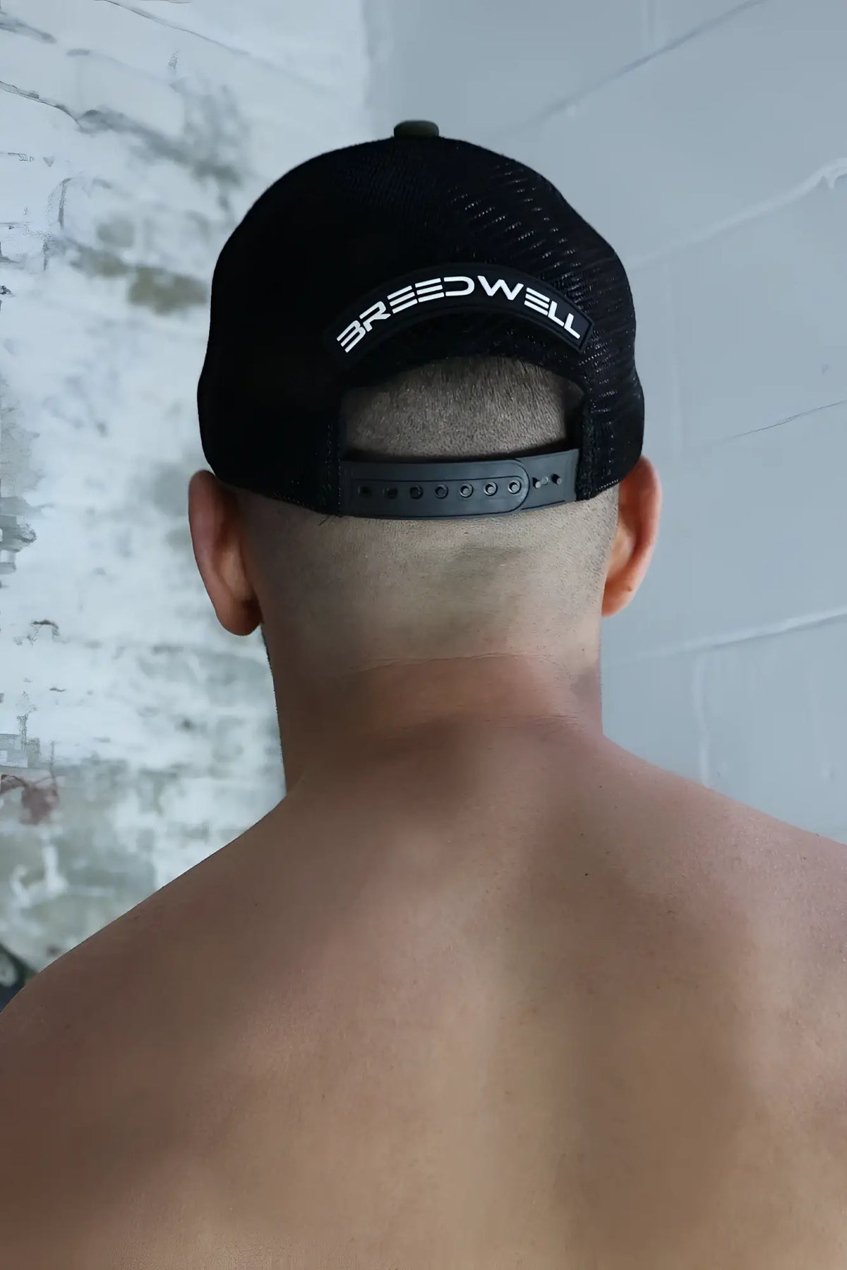 Back view of black mesh dirty trucker hat with white breedwell lettering across the back panel