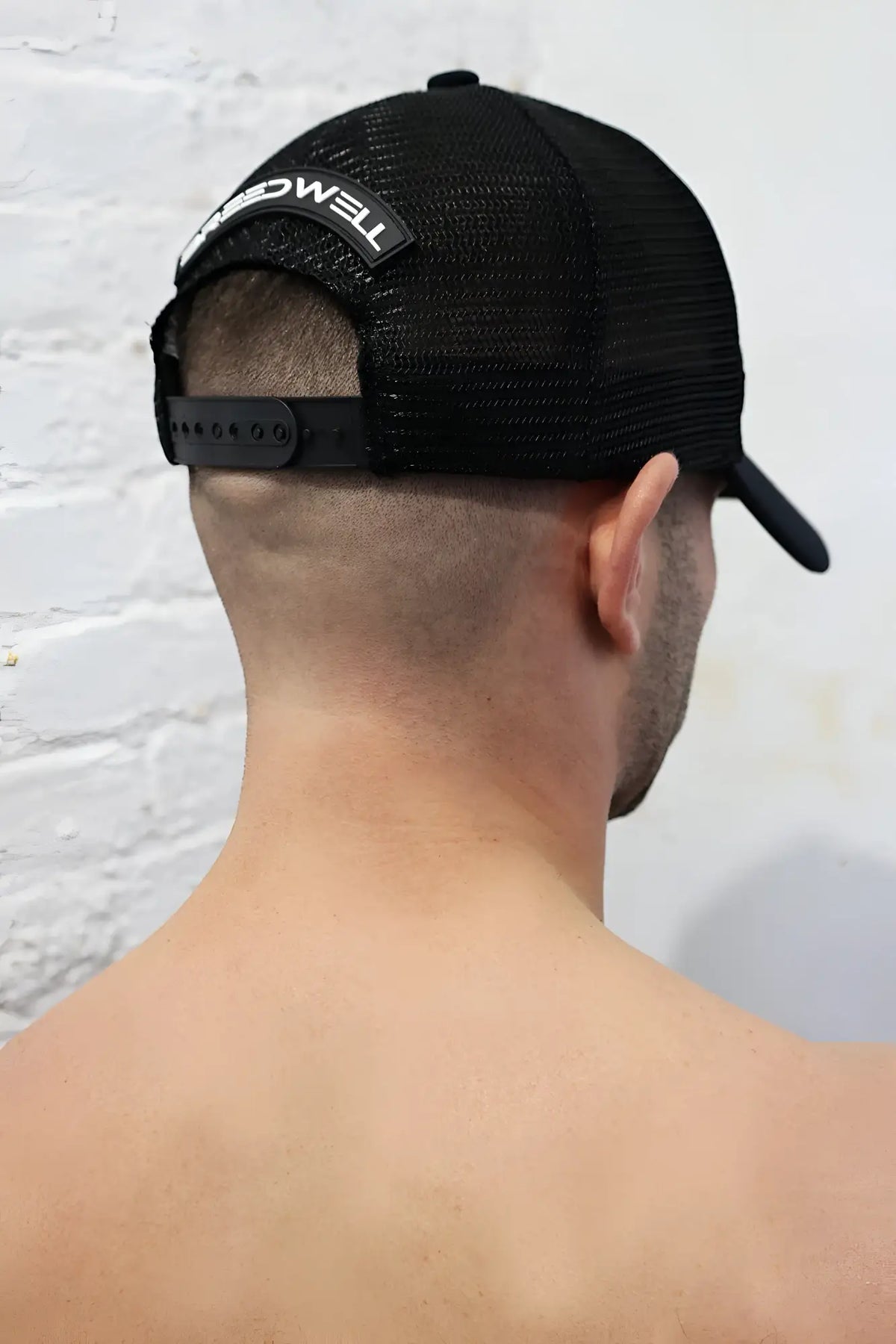 Back side of black mesh dirty trucker hat with white embroidered logo on adjustable strap