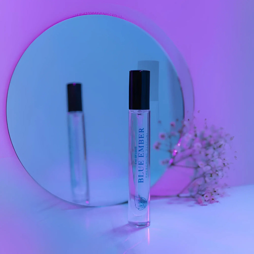A clear glass rollerball perfume bottle with black cap and blue ember text on purple background for attract her use