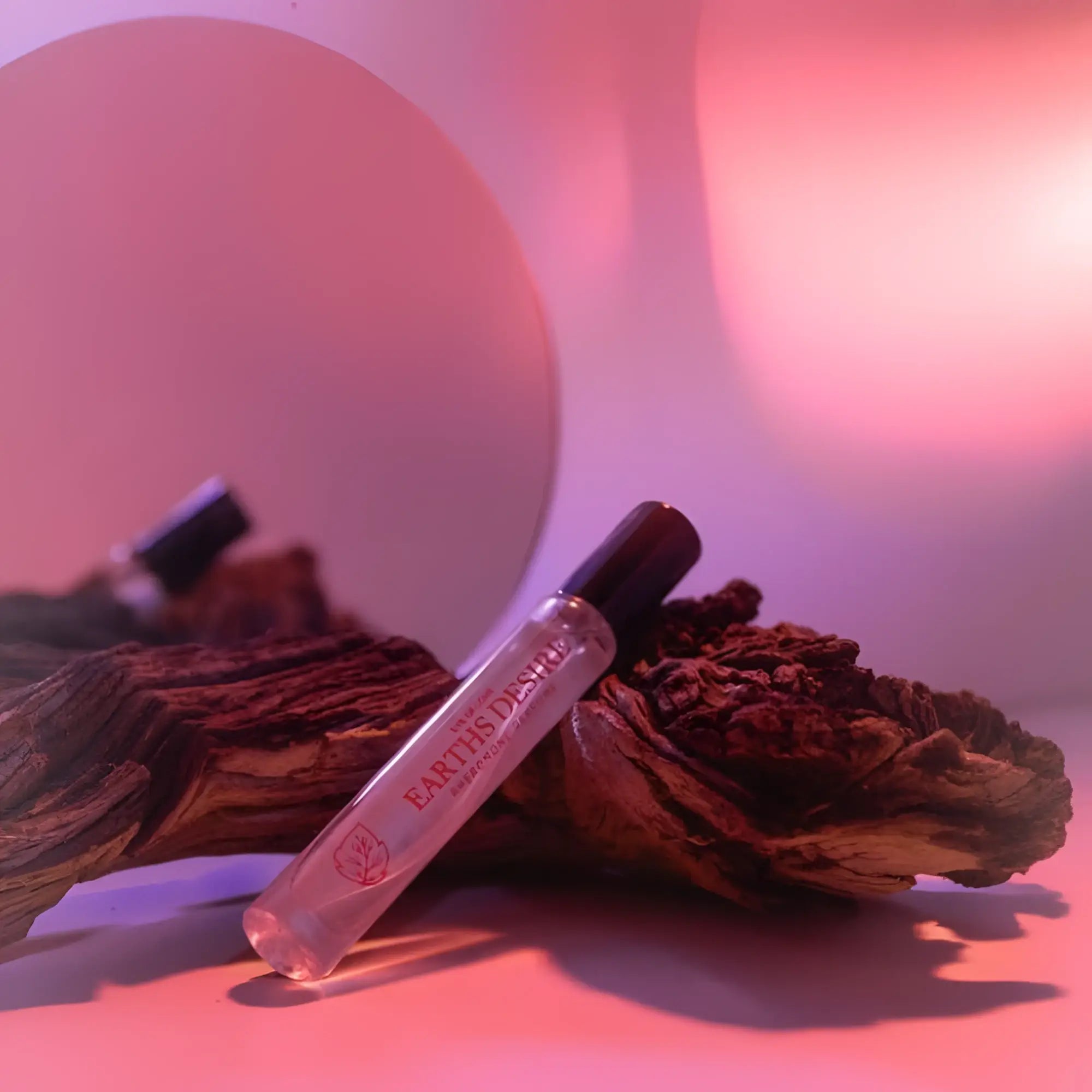 Clear glass rollerball perfume bottle with black cap and red earths desire branding on driftwood for attraction