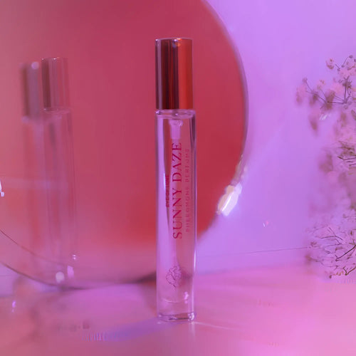 A clear glass roll-on perfume bottle with a metallic gold cap and pink sunny daze text for attracting him