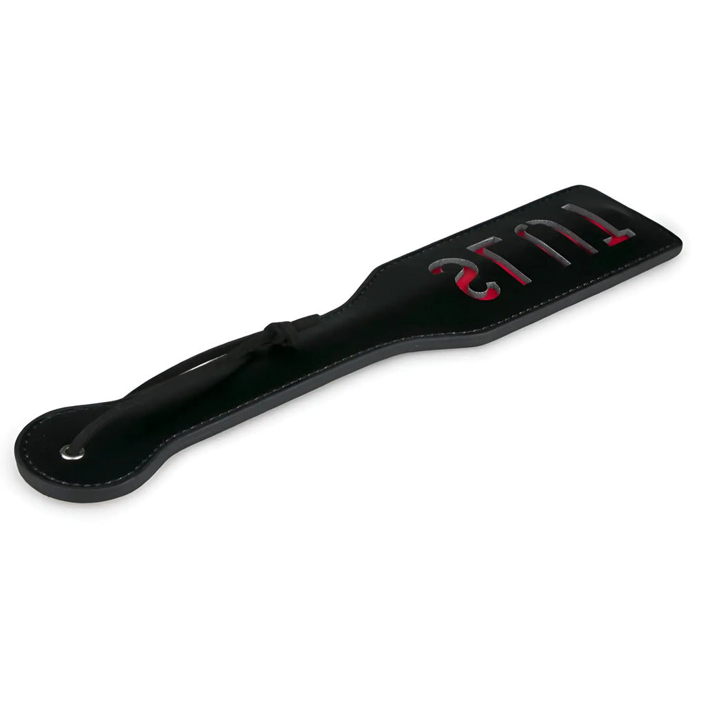 Black leather fetish collection paddle slut with red and silver lettering reading tulis on flat surface