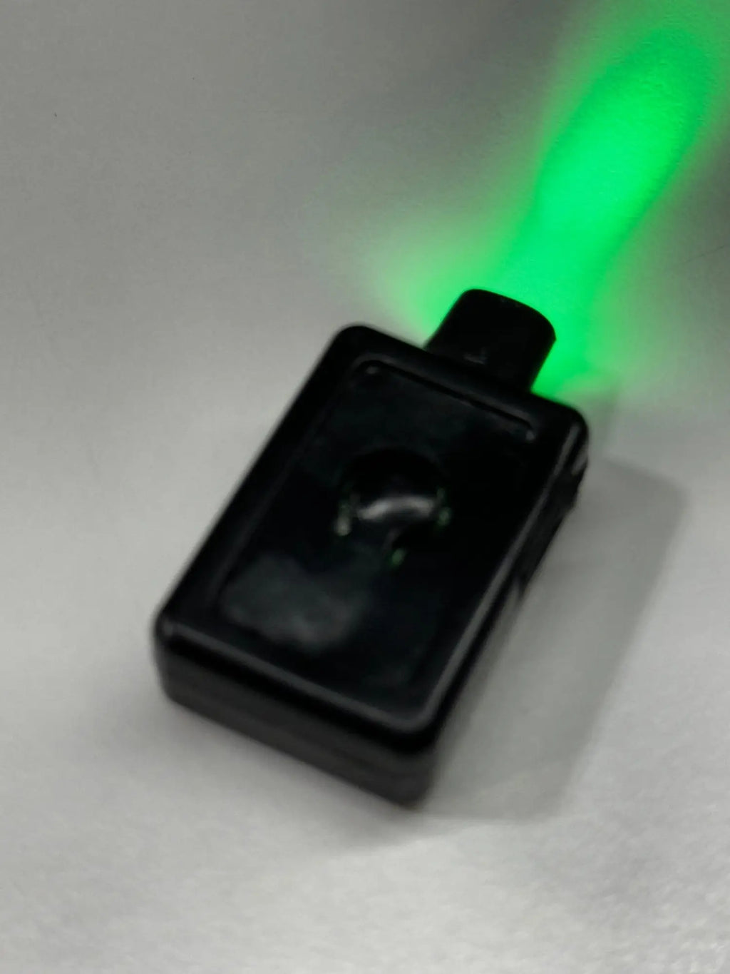 Black rectangular garrison hat battery flashlight emitting a bright green beam for tactical use