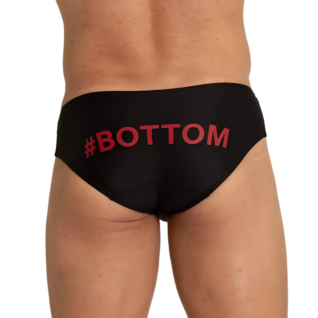 Back side of gigo bottom black swim brief featuring bold red hashtag bottom text on black swim trunks